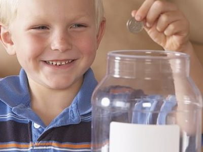 Boy (4-6) putting US coins into donation jar, smiling